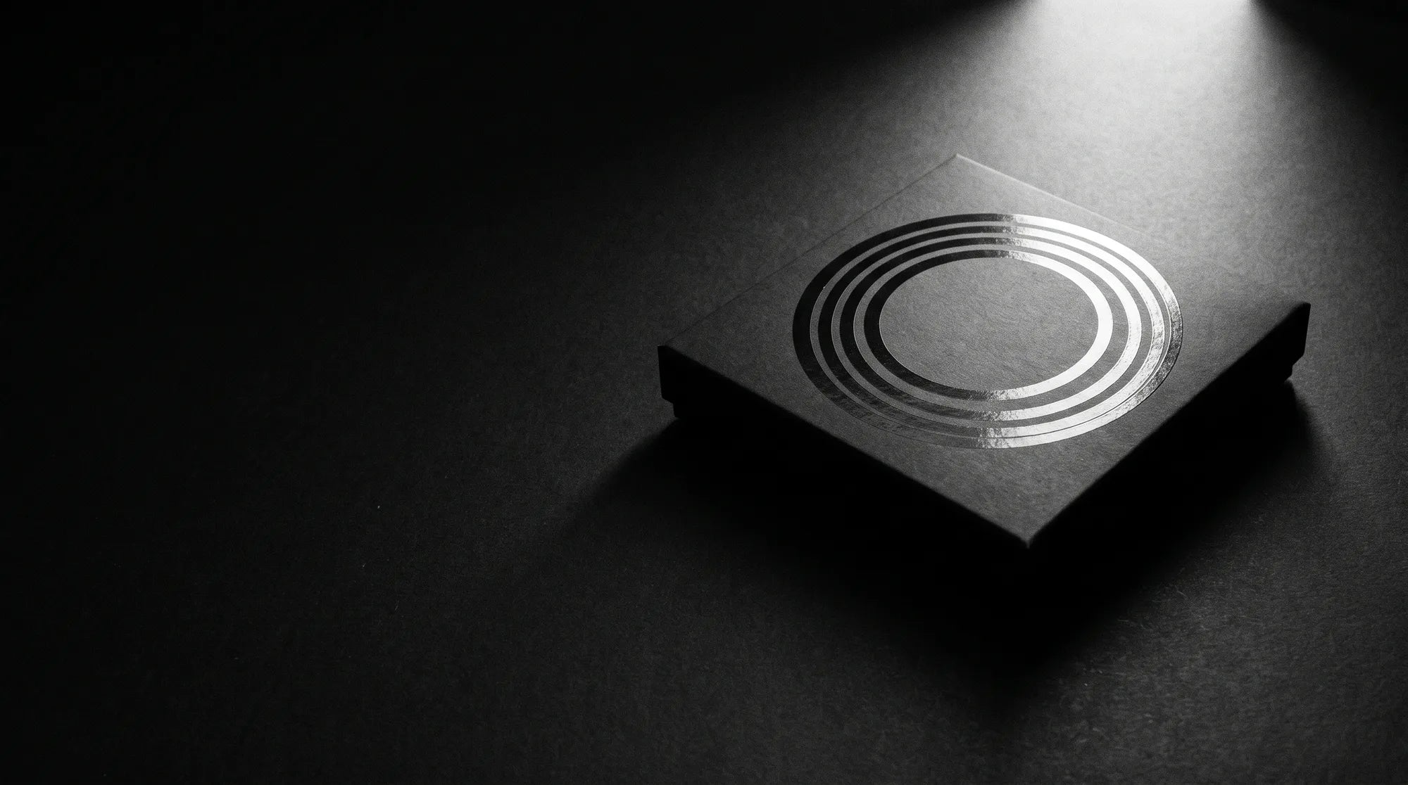 The KC-FIT carton in matte black, its concentric varnish rings caught by a single raking light.